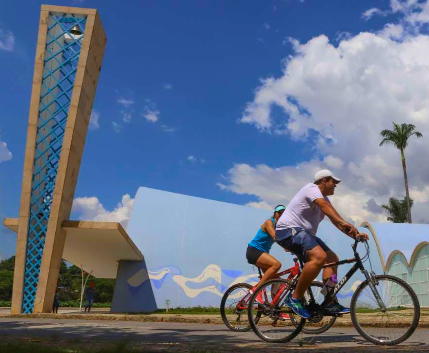 Casal andando de bicicletas bert bike na frente do ponto turistico,igrejinha da pampulha em belo horizonte.